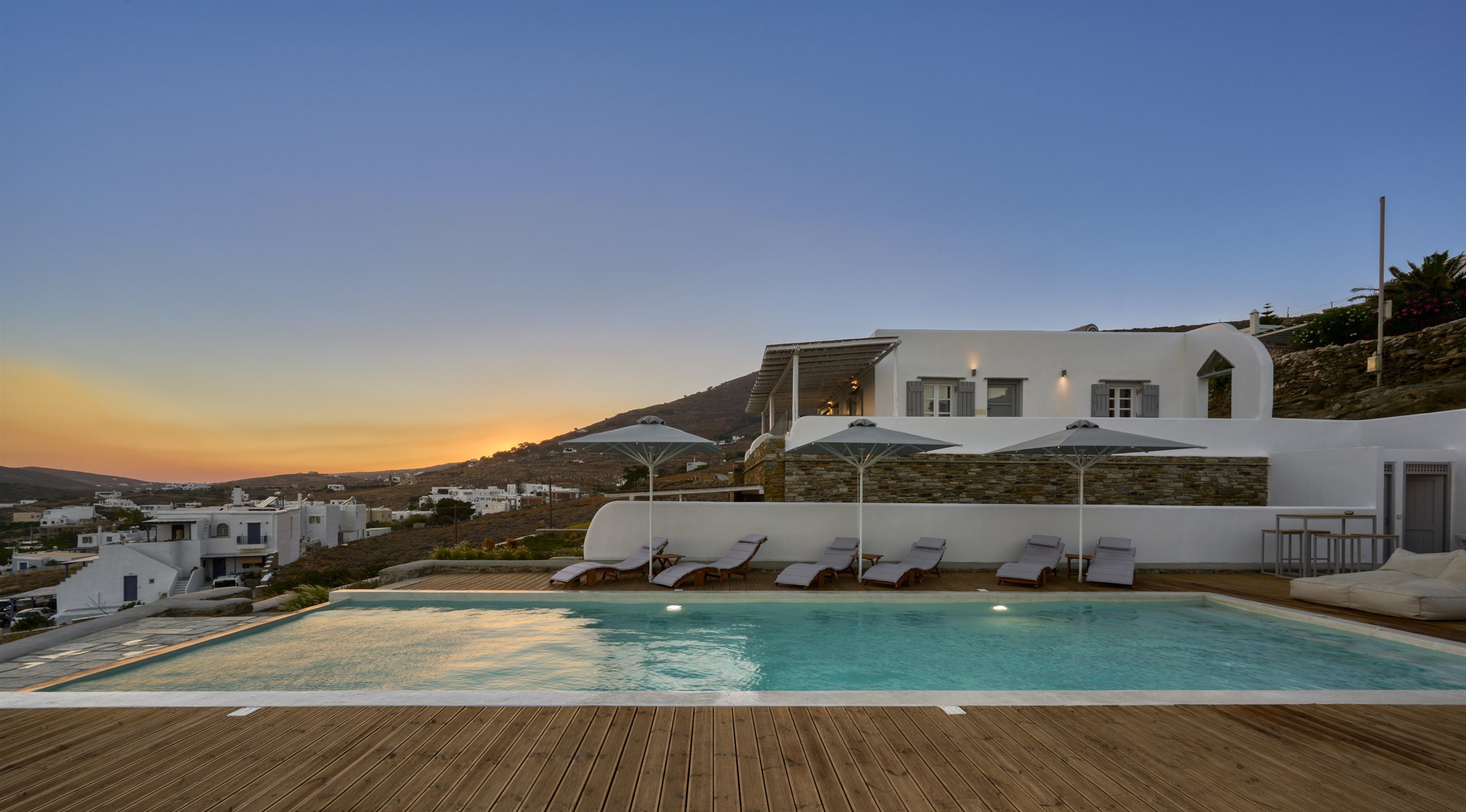 The shared pool at sunset, loungers facing the hills of Tinos